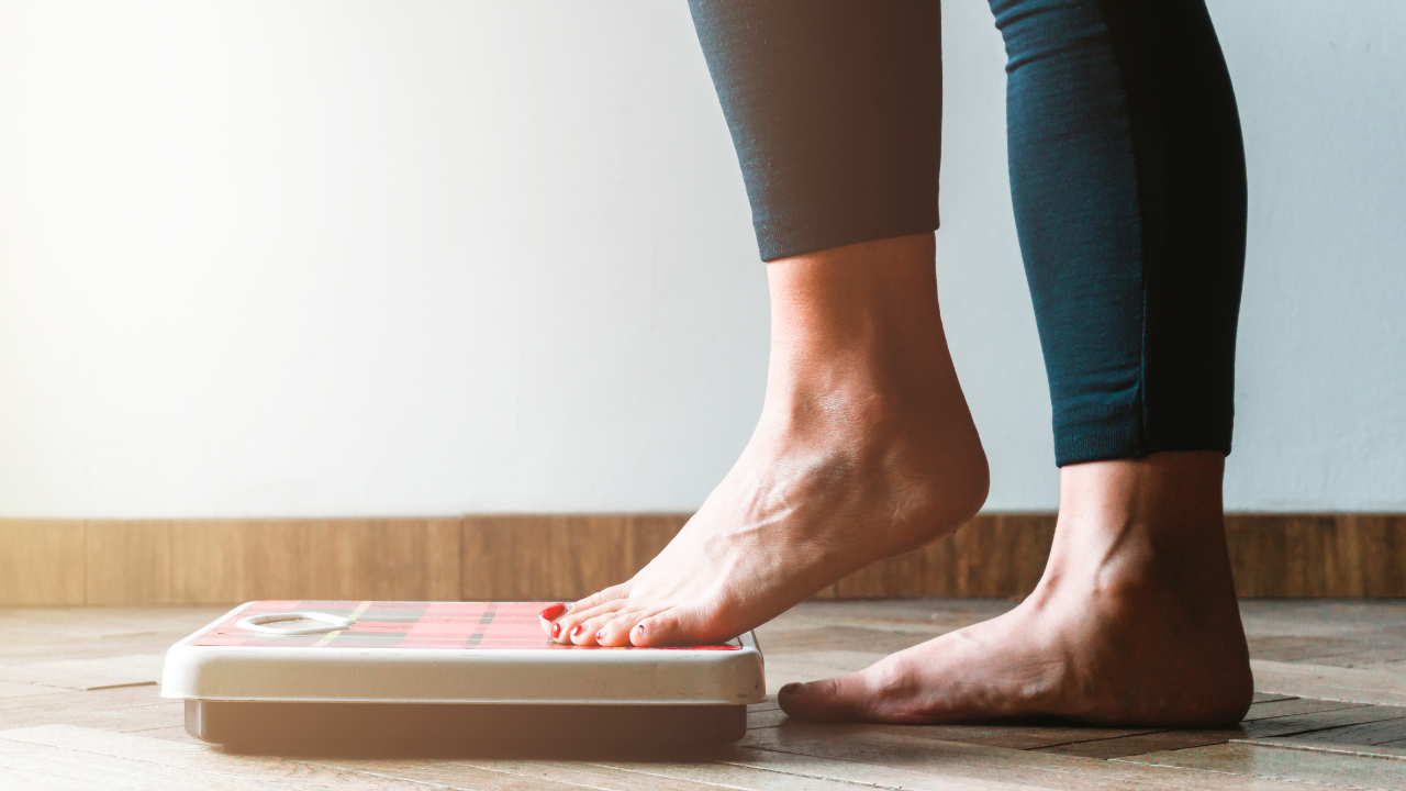 Female checking kilogrammes getting on the scale - self care and body positivity concept - warm flare on left. Image Credit: Adobe Stock Images/Hunterframe