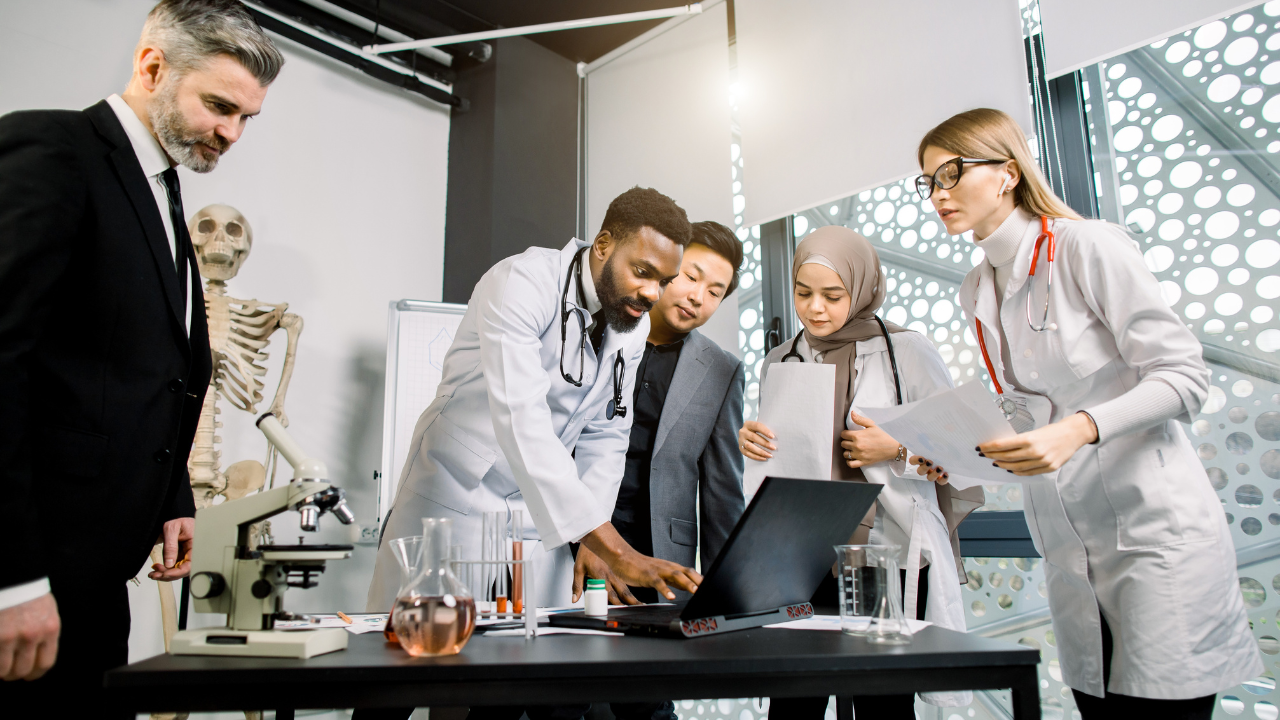 Multiethnic team of doctors, scientists, healthcare workers having a discussion, while using laptop, talking about the results of clinical trial or research. Image Credit: Adobe Stock Images/sofiko14 